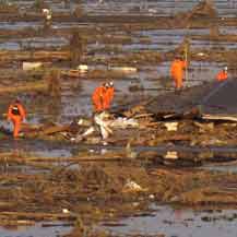 Rescue workers walk on roof of floating house - Japan - photo credit Alex Hofford