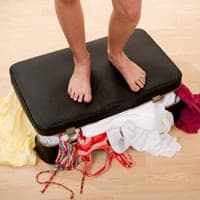 woman standing on an over-full suitcase