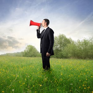 Business man on megaphone, in a field of grass