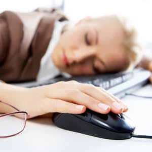 woman asleep on her keyboard, with computer mouse in her hand