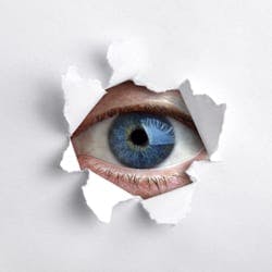 Eye peeping through a hole in white wall